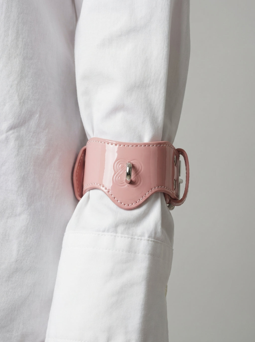 Pink patent leather handcuffs worn over a white shirt for a high-fashion look.