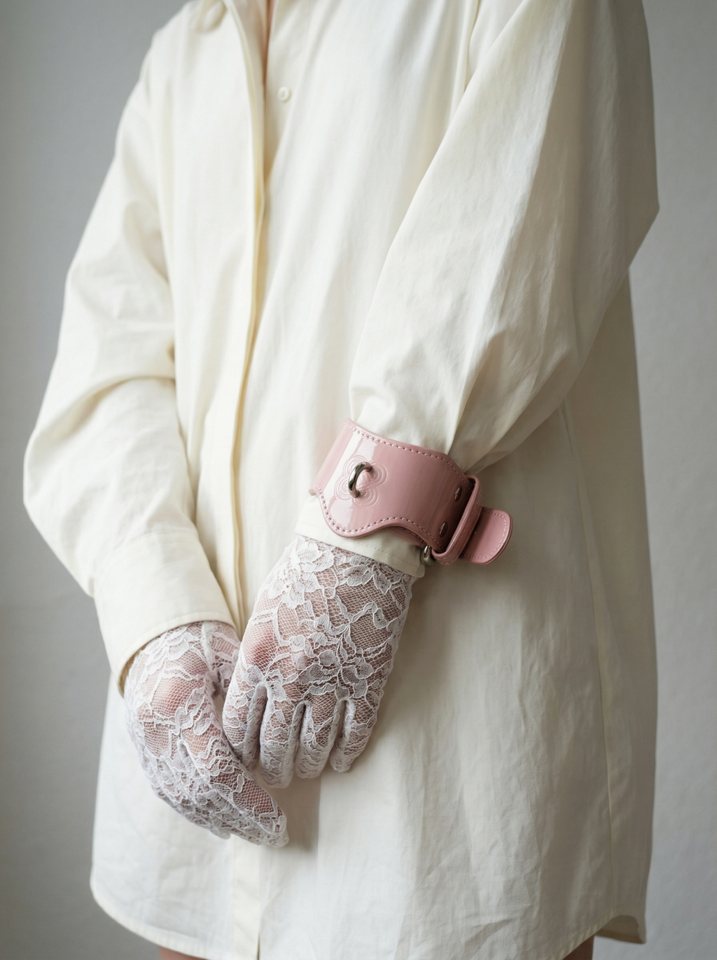 Avant-garde styling: Pink patent leather handcuffs worn over a white shirt for a high-fashion look.